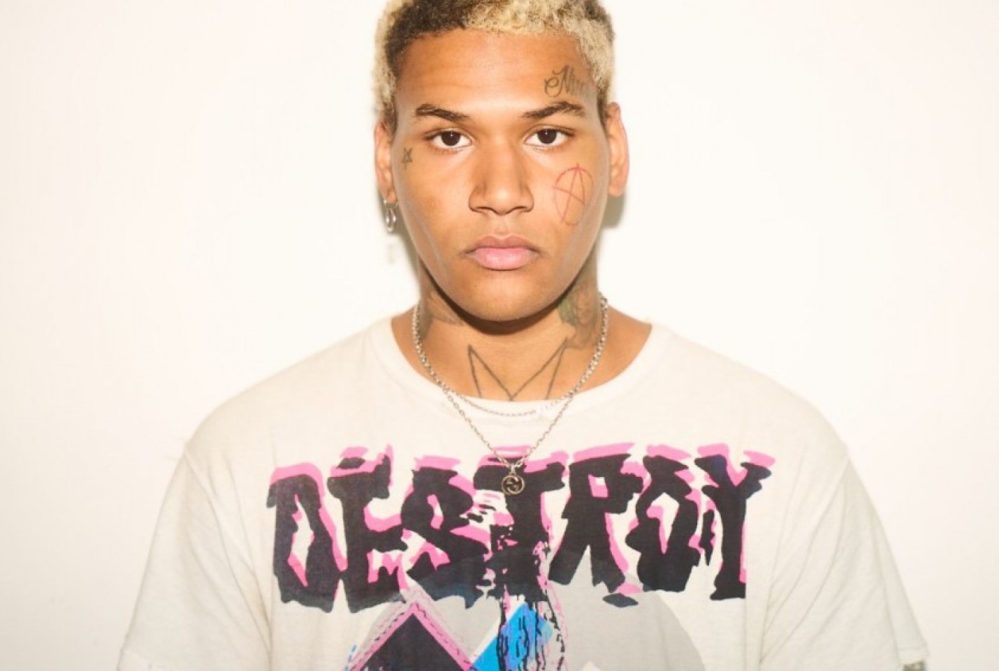 Ekkstacy standing in front of white background with a white patterned t-shirt.